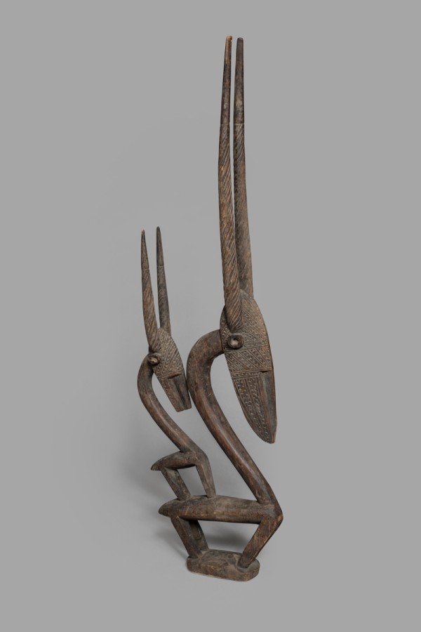 This wooden sculpture represents a chiwara—a mythological hero that is part human, part antelope. It was likely part of a headdress. There are two antelope sculptures with straight horns. One of the sculptures is smaller than the other.