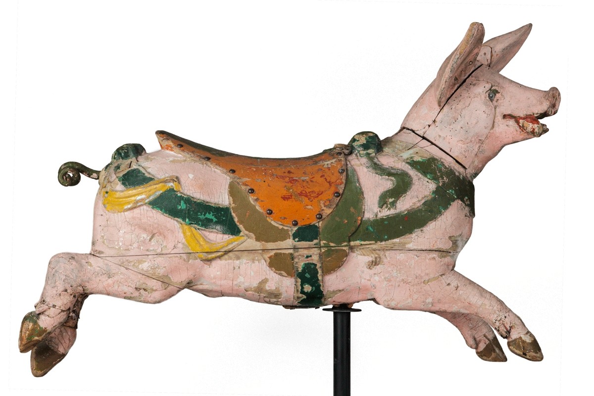 This carousel pig has a pink body with an orange and green saddle attached to its back. The stir-ups are green. It also has a green neck and body collar with yellow ribbon decorating the body collar. The black tail is curled and the pig is in a running form.