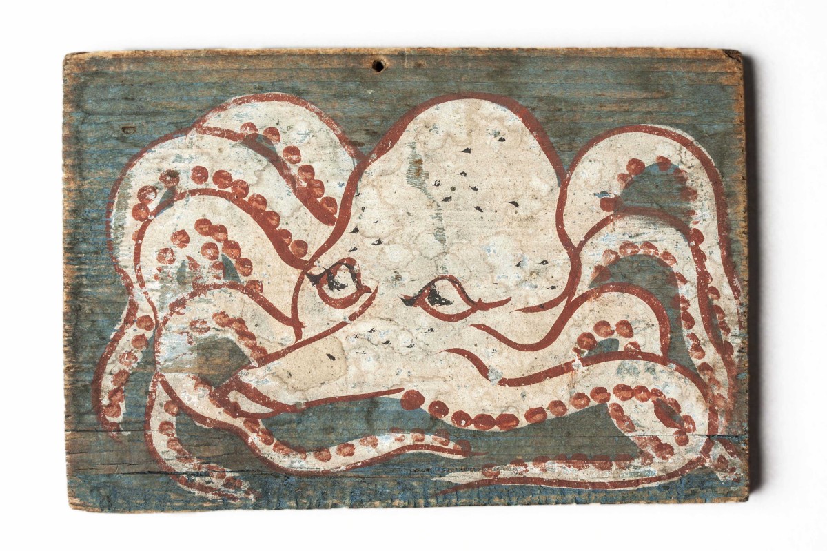 Painted on this ema, a small wooden plaque, is a white octopus with red highlights. The background of is painted light blue.