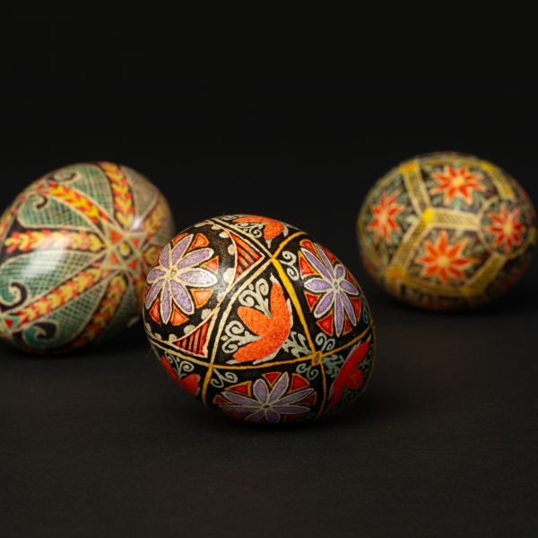 Tana Shane, Pysanky (Ukrainian Decorative Eggs), 20th Century. From Mingei International Museum's Permanent Collection.  

Image Description: three intricately decorated eggs lying on a black background. The patterns on the egg are geometric and include symbols such as stars, flowers, and scrolls. The colors on the eggs include red, purple, yellow, green, and black.
